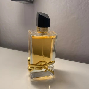 YSL Libre  - Exklusiv parfym från Yves Saint Laurent, Libre Eau de Parfum. Flaskan är rektangulär i genomskinligt glas med guldig detalj och svart asymmetrisk kork. Innehållet är bärnstensfärgat och flaskan pryds av YSL:s ikoniska logga i metall. 90ml. Säljer pga att de ej var en doft för mig, när man tar av locket följer den guldiga med, vilket den inte ska göra men de är pga att de är en spricka i det guldiga (se bild 4)