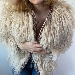 Beige pälsjacka från Zara Basic - Säljer en fluffig beige pälsjacka från Zara Basic med dekorativa broderade kanter i olika färger. Jackan har lång ärm och är perfekt för dig som vill sticka ut med en unik och trendig look.