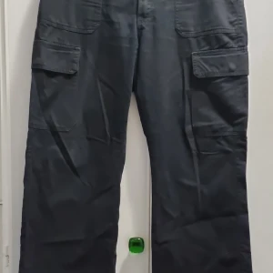 Svarta cargopants med fickor - Svarta cargopants med flera stora fickor på sidorna. Byxorna har en rak passform och är perfekta för en avslappnad stil. Tillverkade i ett slitstarkt material som passar till många olika tillfällen.