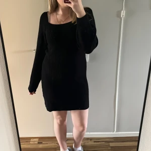 Svart stickad långärmad klänning - Säljer en svart stickad klänning med lång ärm och rundad halsringning. Klänningen är ribbad och har en kroppsnära passform som slutar ovanför knäna. Perfekt för kyligare dagar och enkel att styla med sneakers eller boots.