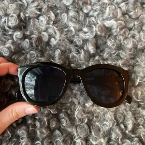 Svarta solglasögon från BikBok - Stilrena svarta solglasögon från BikBok med klassisk rundad form och breda bågar. Perfekta för att ge en cool touch till din outfit. Snygg och tidlös design som passar de flesta.