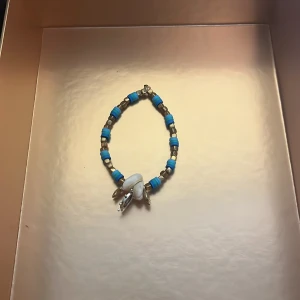 Blått och silverfärgat armband med pärldetaljer - Säljer ett armband med blå och silverfärgade pärlor samt vita pärldetaljer som hänge. Perfekt accessoar för att addera lite färg till din outfit.