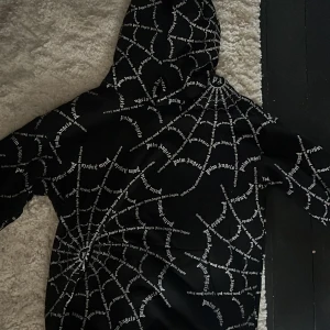 Svart hoodie med spindelnätsmönster från Palm Angels - Säljer en svart hoodie från Palm Angels med unikt vitt spindelnätsmönster och logotyptryck över hela tröjan. Tröjan har huva och är tillverkad i en bomullsblandning. Perfekt för dig som vill sticka ut med streetwear-stil. Pris kan diskuteras.