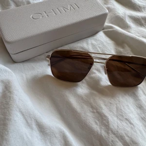 Bruna pilotbågar från CHIMI - Snygga solglasögon från CHIMI med klassisk pilotform och bruna glas. Tunn metallbåge i guld som ger en stilren och modern look. Perfekta för dig som vill ha en tidlös accessoar med lite attityd.