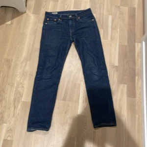 Levi's 502 mörkblå jeans - Säljer ett par klassiska mörkblå Levi's 502 jeans med raka ben och fem fickor. Jeansen har orangea sömmar, knappgylf och den ikoniska läderpatchen bak i midjan. Perfekta för dig som gillar en tidlös och stilren look.