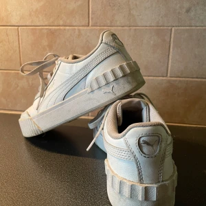 Vita sneakers från Puma - Säljer ett par vita sneakers från Puma med klassisk design och tjock sula. Skorna har snörning och Puma-logga på sidan och hälen. Perfekta för en stilren vardagslook.