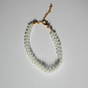 Pärlarmband med guldfärgat spänne - Snyggt och elegant armband med små vita pärlor i dubbla rader och guldfärgat kedjespänne. Perfekt accessoar för att lyfta din stil med en elegant touch eller som en present.