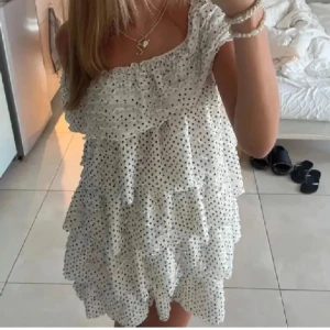 Zara priskrig klänning 💕 - Söt axelbandslös klänning i vitt med svarta prickar och volanger. Klänningen har en luftig passform och flera lager volang, perfekt för varma dagar. Aldrig använt men köpte second hand 