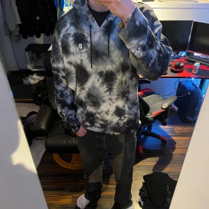Svart och grå tie-dye hoodie från Nike  - Säljer en snygg hoodie från Nike i svart och grå tie-dye. Tröjan har huva med dragsko och en stor magficka. Perfekt för dig som gillar streetwear och vill ha en unik look.
