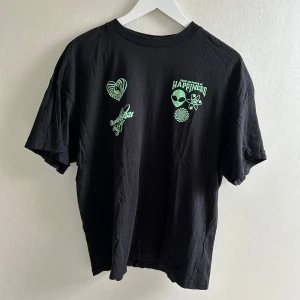 Svart t-shirt med grönt tryck  - Cool svart t-shirt från Divided med gröna tryck framtill. Klassisk passform och rund halsringning🩷