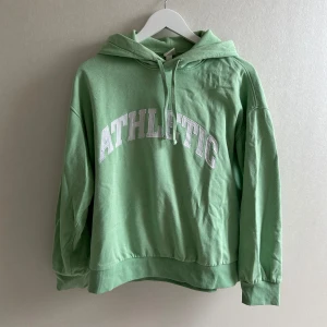 Grön hoodie med tryck - Snygg ljusgrön hoodie med vit text 'ATHLETIC' på bröstet. Tröjan har en luva med snören. Super mysig men är lite nopprig och därav priset. Perfekt att matcha med jeans eller träningsbyxor💗💗
