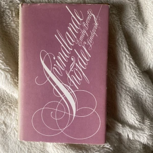 Svindlande höjder - Säljer boken 'Svindlande höjder' av Emily Brontë i svensk översättning. Omslaget är ljust rosa med vit dekorativ text och boken har ett brunt hårt pärmomslag under skyddsomslaget. En klassisk roman om passion och dramatik.