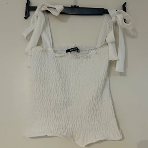 Vit  linnetopp med knytband från Gina Tricot - Supersöt vit linnetopp från Gina Tricot med smockad struktur och breda axelband som knyts i rosetter. Linnet är använt fåtal gånger och är nyskick💞💕