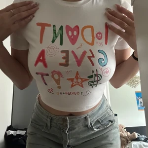 Vit croppad t-shirt med färgglatt tryck - Säljer en vit croppad t-shirt med färgglatt tryck framtill. T-shirten har korta ärmar och en tight passform.