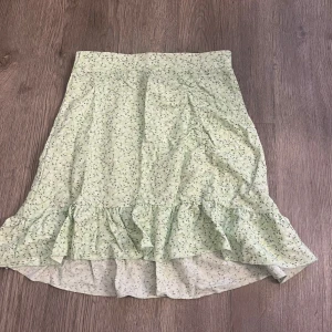 Ljusgrön blommig kjol med volang från Gina Tricot - Supersöt ljusgrön kjol från Gina Tricot med små blommor och volang nertill. Kjolen har en lätt utställd passform och är perfekt för vår och sommar. Tunn och luftig, passar till många olika stilar.