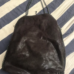 Svart axelväska  - Säljer en svart axelväska med glansig yta och kedjor längs kanterna och som axelrem. 