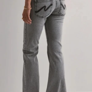 Grå low waist bootcut jeans  - Säljer ett par grå low waist  bootcut jeans från Nelly ,med sömdetaljer på bakfickorna.  Använda några få gånger. Nypris 699