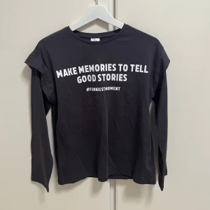 Svart/grå långärmad tröja med text från Zara - Svart/grå långärmad tröja från Zara med vit text på bröstet: 'MAKE MEMORIES TO TELL GOOD STORIES #FUNNIESTMOMENT'. Rund halsringning och rak passform. Perfekt för en avslappnad stil.