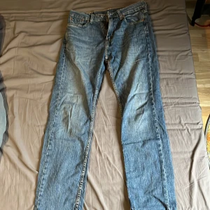 Levis 501 blå jeans - Klassiska blå Levis 501 jeans med raka ben och femficksmodell. Byxorna har knappgylf och den ikoniska Levis-lappen bak i midjan. Perfekta för dig som gillar tidlös denimstil. STORLEK 30 midja 31 längd