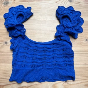 Blå stickad croppad topp med volangärmar - Säljer en blå stickad croppad topp med stora volangärmar och vågigt mönster. Perfekt för dig som vill sticka ut med en färgglad och unik topp. Supersnygg till både jeans och kjol! 