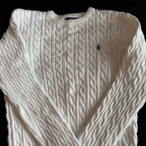 Vit kabelstickad tröja från Ralph Lauren - Säljer en klassisk vit kabelstickad tröja från Ralph Lauren med rund halsringning och broderad logga på bröstet. Tröjan har lång ärm och är perfekt för en stilren och tidlös look.