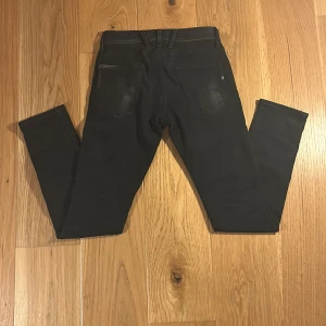 Svarta Replay jeansbyxor herr - Svarta jeansbyxor från Replay med klassisk femficksdesign och Replay-logga på bakfickan. Byxorna har normal passform och raka ben. Midjemått W30 och längd 32. Perfekta för dig som gillar stilrena och tidlösa jeans.