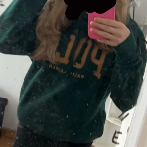 Grön sweatshirt från Ralph Lauren - Mörkgrön sweatshirt från Ralph Lauren med stor gul POL-tryck på bröstet. Klassisk rund hals och långa ärmar. Perfekt för en avslappnad stil.
