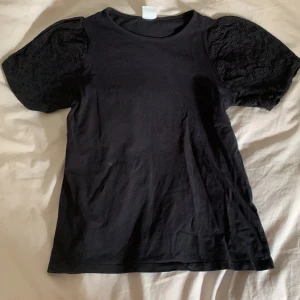 Svart topp med puffärmar från Zara - Svart topp från Zara med snygga puffärmar i broderad bomull. Ärmarna har ett coolt hålmönster som ger en extra touch till looken. Klassisk rund halsringning och rak passform. Perfekt för dig som vill ha en basic topp med något extra.