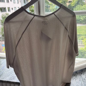 Vit mesh t-shirt från MQ i XL - Vit mesh t-shirt från MQ med kort ärm och sportig vibe. T-shirten är tillverkad i ett tunt, genomskinligt syntetmaterial som andas och har en clean look med diskret logga i nacken. Perfekt för dig som gillar minimalistisk och modern stil.