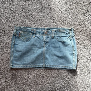 Levi's ljusblå jeanskjol Jenny Mae - Supersnygg ljusblå jeanskjol från Levi's, modell Jenny Mae. Klassisk femficksdesign med snygga detaljer och Levi's-märke framtill. Kjolen är kort och midjemått är 40cm och längden 27,5cm