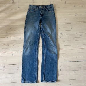 Blå raka jeans från Zara, strl 32 - Klassiska blå jeans från Zara i rak modell med fem fickor och normal passform. Jeansen har hög midja och är tillverkade i bomullsdenim. Snyggt slitna detaljer nertill på benen för en avslappnad vibe.