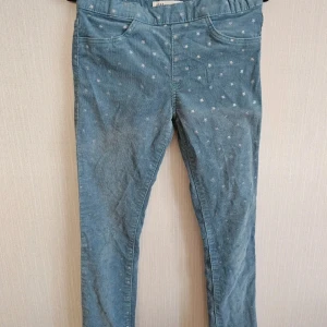 Blå byxor med små stjärnor 122 - Blåa byxor med massa små stjärnor.  En liten fläck bak jämte fickan, ett litet trådsläpp bak, lite slitage syns fram på låren