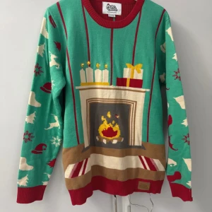 Grön jultröja med öppen spis från Silly Santa - Rolig grön jultröja från Silly Santa med motiv av öppen spis, ljus och paket framtill. Ärmarna har mönster med tomteluvor, snöflingor, renar och granar. Röd ribbad hals, ärmslut och nederkant.  Storlek medium Dam /storlek Small Herr
