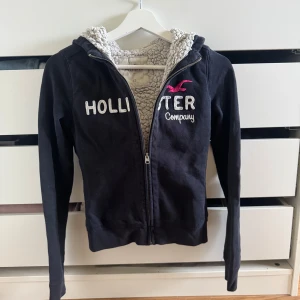 Marinblå zip up hoodie från Hollister - Marinblå zip up hoodie med foder från Hollister, broderad logga och text på bröstet i vitt och rosa. Mjuk insida!🩷