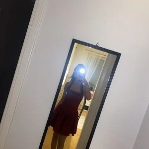 Röd kort klänning med volang - Supersöt röd kortklänning med volang nertill och breda axelband. Klänningen har en tight passform upptill och en utställd kjol, perfekt för dig som vill sticka ut. Enkel men ändå riktigt snygg design.