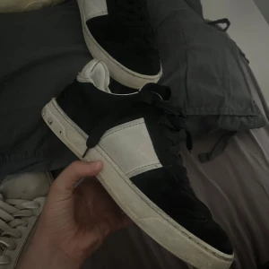 Valentino Garavani sneakers svart/vit - Snygga sneakers från Valentino Garavani i svart mocka och vitt skinn. Klassisk låg modell med svarta skosnören och coola nitar på hälen. Sulan har ett unikt mönster undertill. Perfekta för dig som gillar streetstyle med lyxig touch. De är jätte fina skor men har tyvärr lossnat lite framme vid sidan av tårna men de är limmat! De syns på bilderna. Är i stolek 37 men passar en storlek större! Skivka pris förslag för jag vet inte riktigt vad jag ska sälja dessa för!