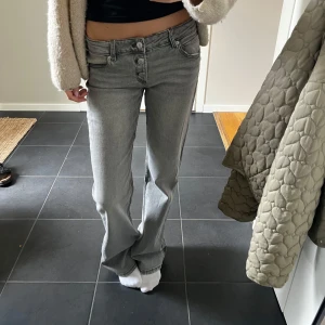 Grå bootcut, lowwaist jeans från  - Snygga grå jeans från Gina Tricot i bootcut-modell med låg midja. Jeansen har klassisk femficksdesign, flera knappar i gylfen. Det finns spännband innanföf för att kunna spänna eller lätta midjan.