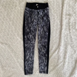 Stronger träningsbyxor - Snygga leggings från Stronger i storlek S med svart och grått mönster framtill och svarta partier på sidorna och baksidan. Hög midja och stretchigt material i polyester och elastan gör dem perfekta för träning eller chill.
