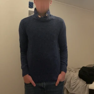 Blå stickad tröja från L.O.G.G. - Mysig mörkblå stickad tröja från L.O.G.G. med hög krage och snygga träknappar vid halsen. Tröjan har lång ärm och ribbade muddar för en skön passform. Perfekt för kyliga dagar och enkel att matcha med jeans.