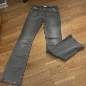 Grå raka jeans med fickdetaljer - Snygga grå jeans med raka ben och klassisk femficksdesign. Baktill finns två fickor med lock och knappdetalj som ger en cool touch. Jeansen har bälteshällor och är tillverkade i ett mjukt bomullsmaterial. Perfekta för en avslappnad och stilren look.