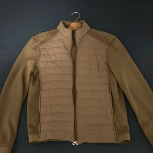 Beige quiltad jacka med dragkedja - Snygg beige jacka med quiltad front och släta ärmar. Jackan har hög krage och hel dragkedja framtill. Perfekt för dig som gillar stilren och enkel design. Passar till många olika outfits och har en modern look.