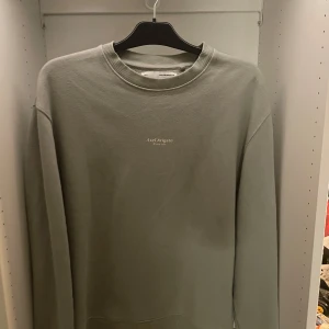 Grå sweatshirt från Axel Arigato - Snygg grå sweatshirt från Axel Arigato med minimalistisk logga tryckt på bröstet. Tröjan har rund halsringning, ribbade muddar och är långärmad. Perfekt för en clean och stilren look. Materialet är mjuk bomull som känns skönt mot huden. Aldrig använd