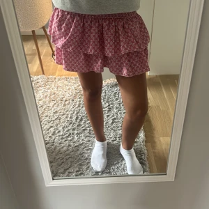 Rosa volangkjol från Meet x Tiger - Supersöt rosa kortkjol med vita blommönster från Meet x Tiger. Kjolen har två volanger och en smockad midja som sitter bekvämt. Köpt från meet me there, köpte för ungefär 450