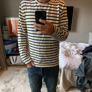 Randig långärmad tröja från Arket - Säljer en klassisk långärmad tröja med marinblå och vita ränder. Tröjan har en avslappnad passform och är gjord i mjuk bomull, perfekt för dig som gillar en enkel men stilren look. Passar lika bra till jeans som till shorts. 