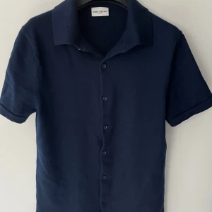 Mörkblå kortärmad Merinoull piké John Henric - Snygg mörkblå Piké från John Henric i storlek S men passar XS. Skjortan har korta ärmar, klassisk krage och knäppning framtill. 