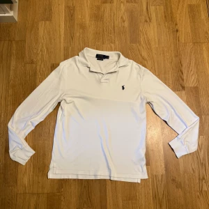 Vit långärmad piké från Ralph Lauren - Vit långärmad pikétröja från Polo Ralph Lauren med klassisk krage och två knappar vid halsen. Tröjan har den ikoniska broderade loggan på bröstet och är i en slim fit-modell. Perfekt för dig som gillar stilrena och tidlösa plagg. Storlek s men sitter som xs 