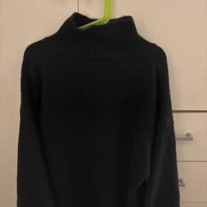 Svart polotröja med hög krage - Mysig svart polotröja med hög, ribbad krage och lång ärm. Perfekt för kalla dagar och enkel att matcha med olika outfits. Tröjan har en klassisk och stilren look som funkar året runt.