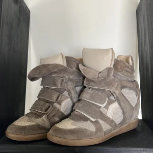 Isabell marant skor - Coola wedge sneakers från Isabel Marant i beige mocka och skinn. Skorna har flera kardborreband, rund tå och platt gummisula. Den dolda kilklacken ger extra höjd och streetstyle-vibe. Perfekta för dig som vill ha en edgy look med bekväm känsla.