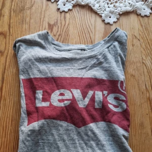 Grå Levi's t-shirt med röd logga - Snygg grå t-shirt från Levi's med den klassiska röda loggan tryckt framtill. T-shirten är kortärmad och har en rund halsringning. Perfekt för dig som gillar en enkel men ikonisk streetstil.