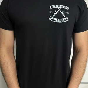 Svart Askari Fight Wear t-shirt - Svart t-shirt från Askari Fight Wear med stort vitt tryck både fram och bak. Trycket har texten 'ASKARI FIGHT WEAR' och två korsade gevär. Klassisk passform och rund hals, perfekt för dig som gillar streetwear och kampsport.